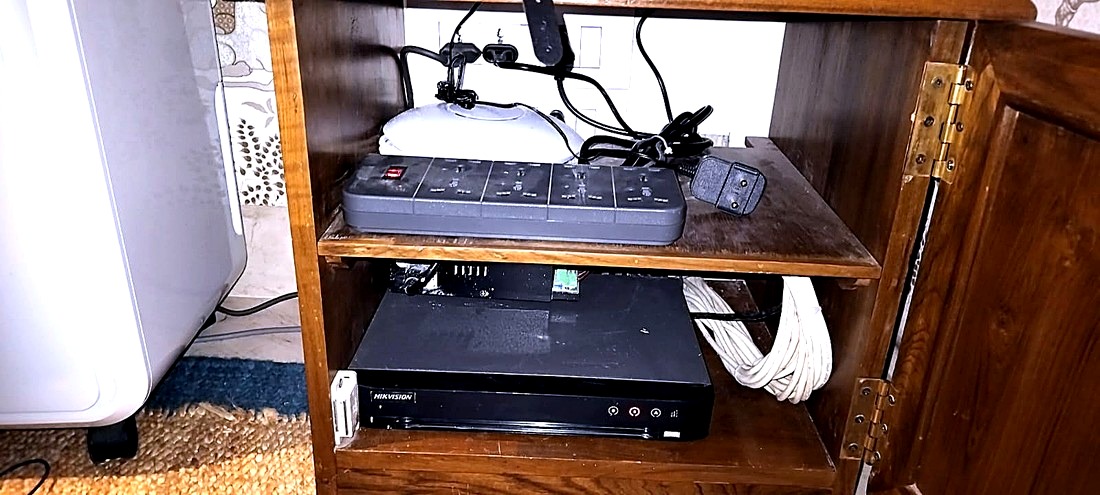 After: a Hikvision recorder seated on a cabinet shelf with the surplus cable coiled and tied beside it.